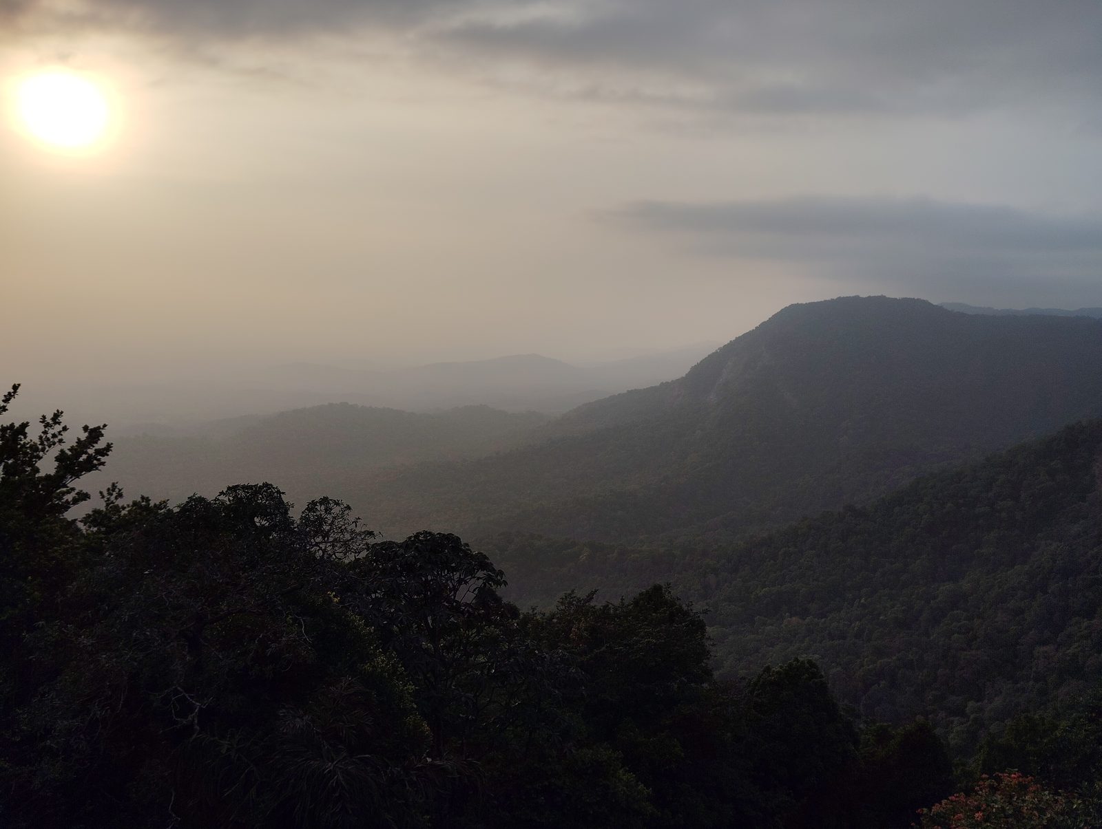 Coucher de soleil voilé sur les collines d'Agumbe : une crête sombre se dresse au-dessus de la brume